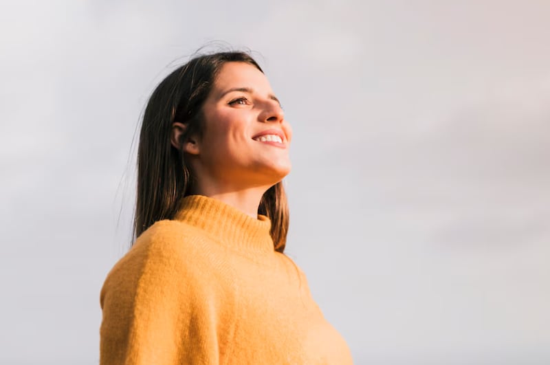 Mujer joven sonriente que se opone al cielo que mira lejos.