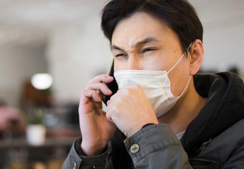 Vista lateral del hombre tosiendo en máscara médica mientras habla por teléfono