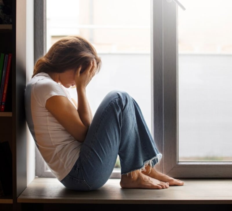 Retrato de mujer joven con baja autoestima sentada junto a la ventana en casa