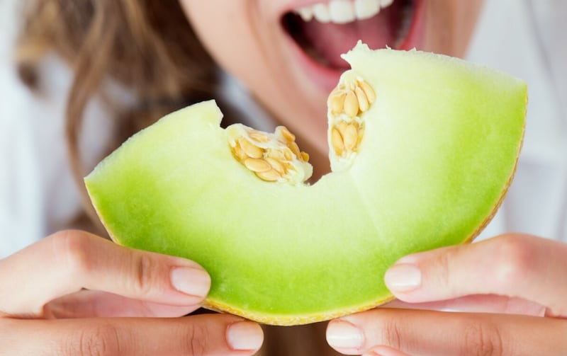 Mujer joven en ropa interior comiendo melón. Aislado en blanco